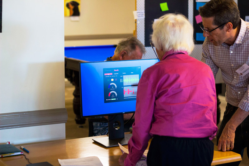 Elderly woman using desktop computer to participate in research, assisted by researcher.