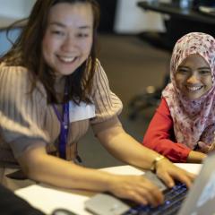 two young women smiling using an open laptop